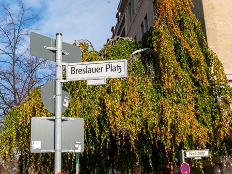 Ein Straßenschild mit der Aufschrift "Breslauer Patz". Im Hintergrund sind Bäume und ein blauer Himmel zu sehen.