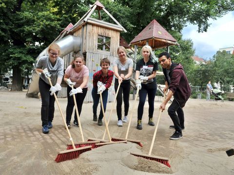 Pressefoto PULS-Camp 2023 - Sechs unterschiedliche Jugendliche kehren gemeisam Sand in die Fugen eines neu verlegten Pflasters auf einem Spielplatz