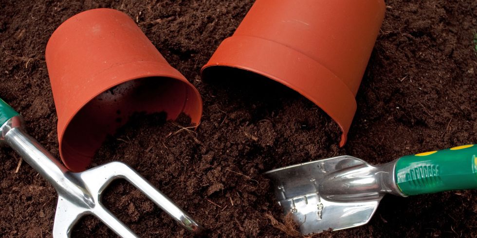 Eine kleine Schauffel und eine Harke liegen neben 3 Blumentöpfen auf dunkler Blumenerde