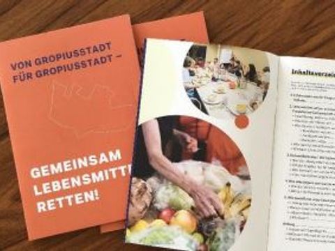 Eine Broschüre mit der Aufschrift Von Gropiusstadt, für Gropiusstadt - gemeinsam Lebensmittel retten! liegt auf einem Holztisch