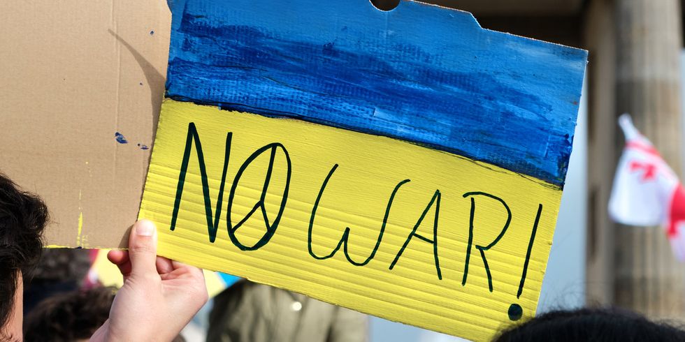 Packard mit dem Schriftzug No War mit pazifischem Zeichen, ukrainisch-gelb-blaue Flagge in der Hand, dahinter das Brandenburger Tor. Protest gegen den Krieg in der Ukraine in der Mitte Berlins