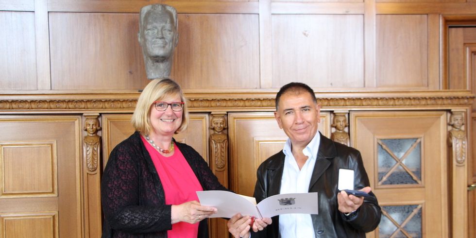 Eine Frau übergibt einen Mann eine Urkunde und Medaille