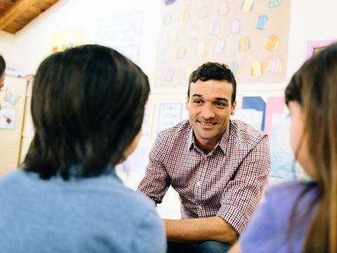 Ein Lehrer sitzt drei Schülerinnen gegenüber und spricht