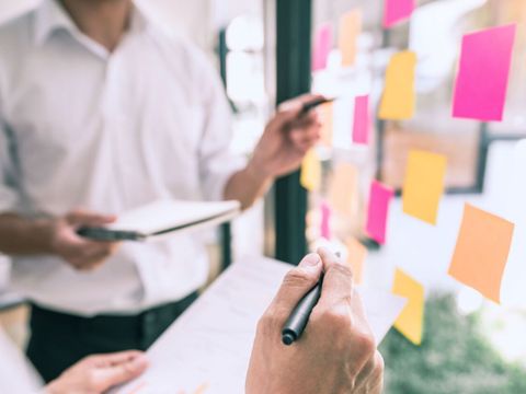 2 Menschen stehen vor einer Scheibe auf der bunte Notzzettel geklebt sind