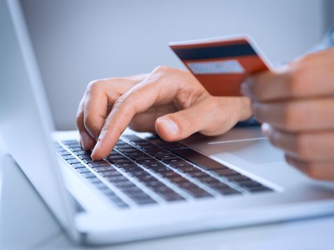 Eine Person hält mit der linken Hand eine Chipkarte vor sich und tippt mit der rechten Hand auf der Tastatur eines Laptops