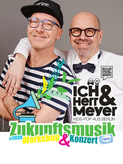 ICH & HERR MEYER (zwei Männer mittleren Alters) lächeln in die Kamera. Beide tragen Brillen, der größere eine Mütze