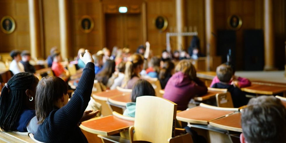 In einem großen Saal mit Stühlen und Tischen sitzen Jugendliche.