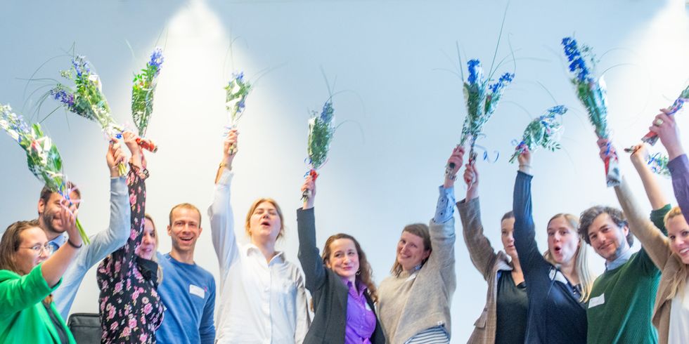 Die Teilnehmer*innen des K+-Führungskräfteprogramms halten Blumensträuße in die Luft