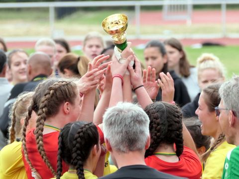 Ein Mädchenteam jubelt und streckt den gewonnenen Pokal in die Höhe.