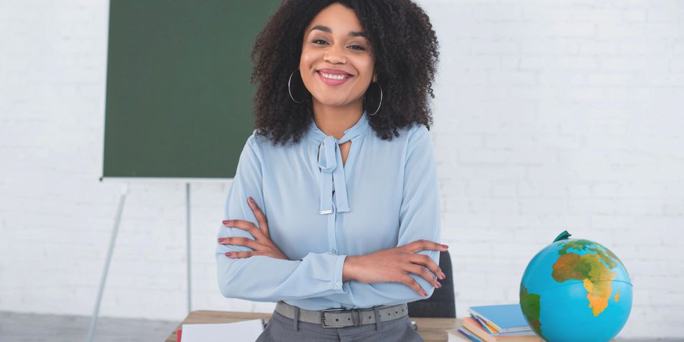Afikanische Lehrerin lehnt lächelnt am Lehrerpult