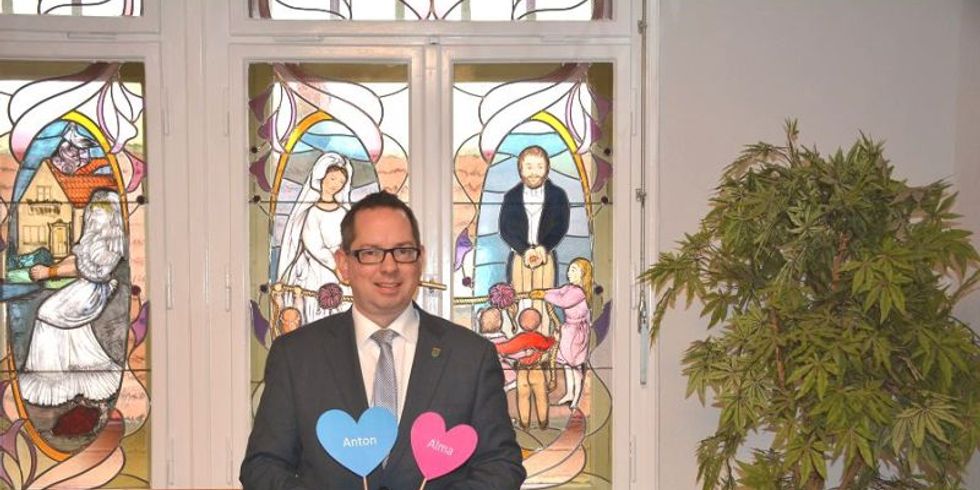 Bezirksbürgermeister Igel hält 2 Schilder mit den beliebtesten Vornamen 2018 in die Kamera. Alma und Anton.