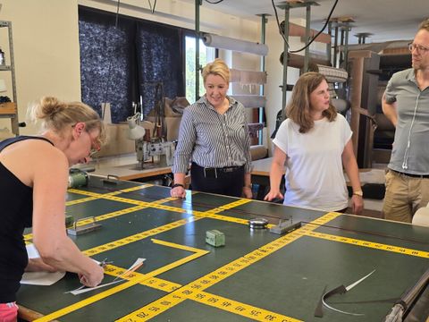 Wirtschaftssenatorin Franziska Giffey, Bezirksbürgermeisterin Clara Herrmann und Baustadtrat Florian Schmidt mit einer Mitarbeiterin der Polsterei Surma am Schneidetisch