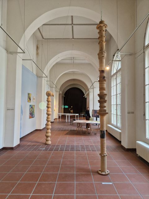 Innenansicht der Galerie im Körnerpark: Holzturm-Skulpturen und Bilder an der Wand