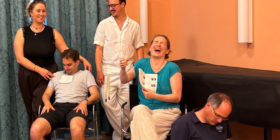 5 Menschen proben fröhlich einen Opernauftritt auf einer Bühne.