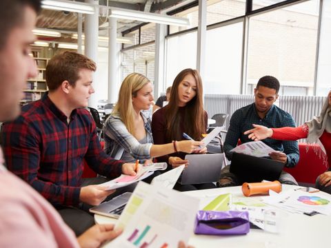 Gruppe Studenten sitzt an einem runden Tisch und macht Projektarbeit