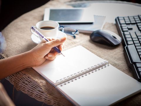 Hand, die am Tisch schreibt mit Tastatur, Maus, Tablet, Kaffeetasse