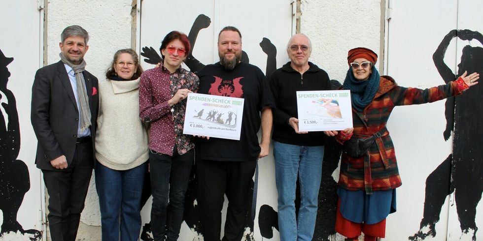 Sechs Personen stehen zusammen und halten zwei Spenden-Schecks in den Händen.
