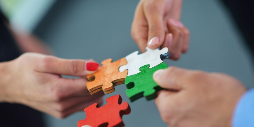 Hände stecken vier Puzzleteile zusammen