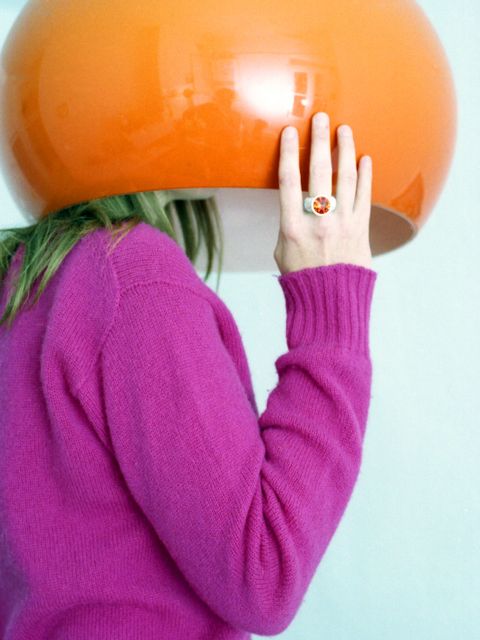 Frau versteckt Kopf unter großem, orangenem Lampenschirm