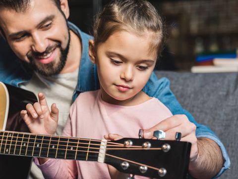 ein Mann zeigt einem kleinen Mädchen das Gitarre spielen
