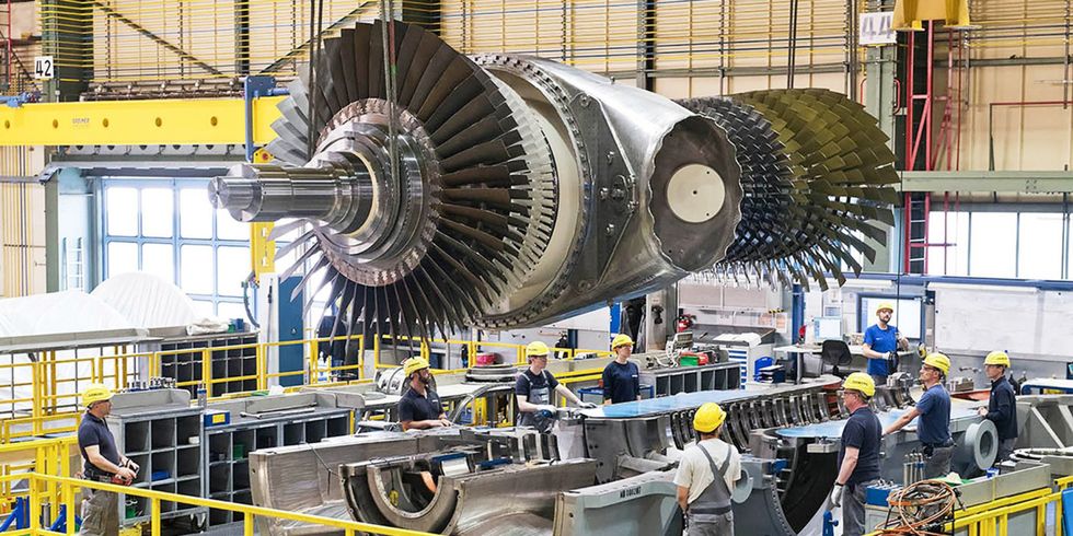 ein Kran hält ein großes Turbinentriebwerk in der Luft einer Fertigungshalle