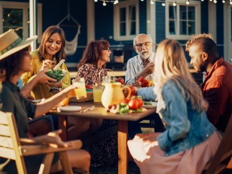 Eltern, Kinder und Freunde versammelten sich an einem Grilltisch vor einem schönen Haus. Menschen unterschiedlicher Herkunft, Jung und Alt, hatten Spaß, aßen und tranken. Eine Gartenparty im Hinterhof.
