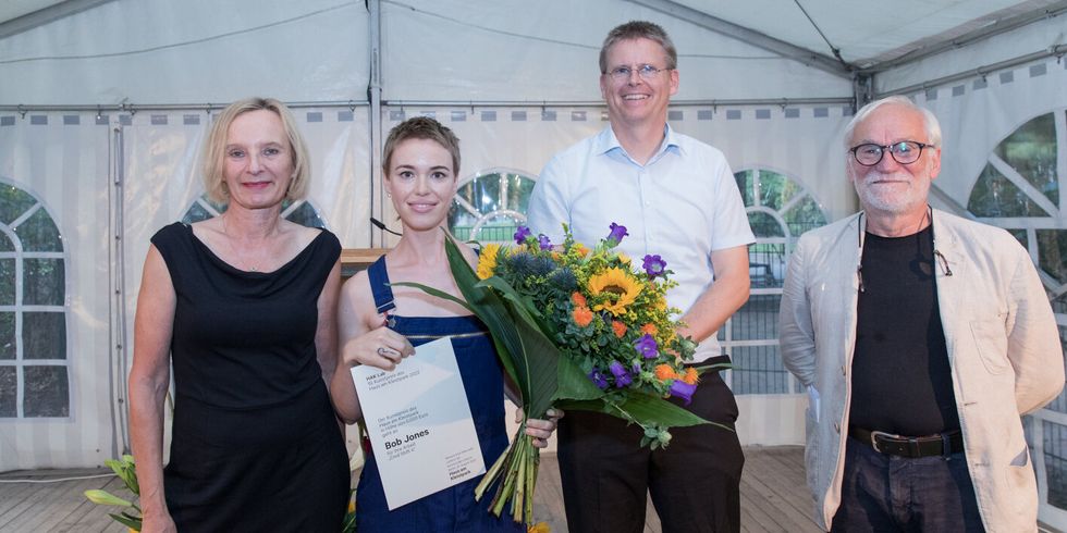 Eine Frau mit Urkunde und einem großen Blumenstrauß mit drei weiteren Personen