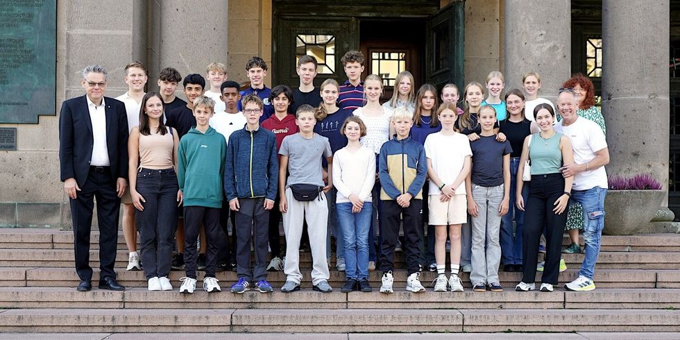 Eine Gruppe von Jugendlichen und wenigen Erwachsenen auf der Treppe am Eingang eines Gebäudes.