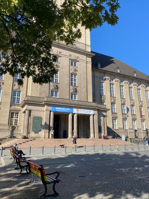 ein Platz mit farbigen Sitzbänken vor eine großen Gebäude