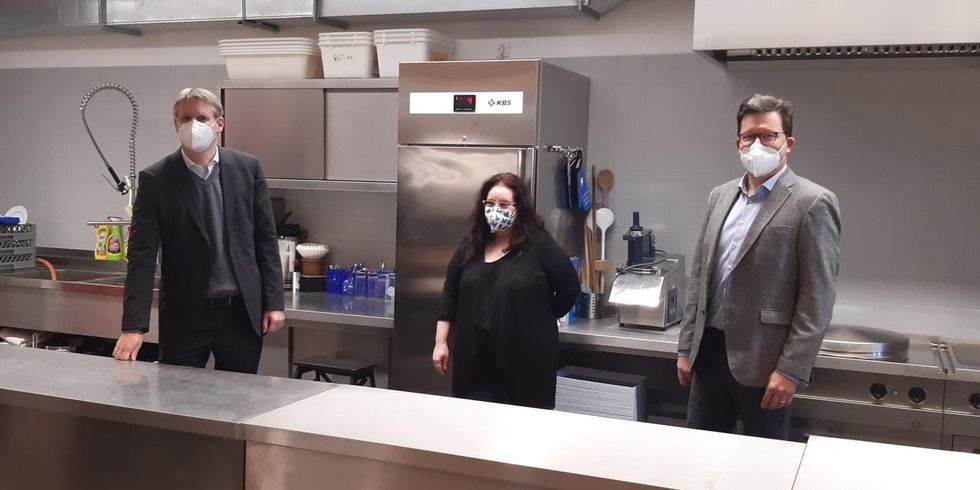 Drei Personen stehen hinter einer Theke in einer modernen Küche.