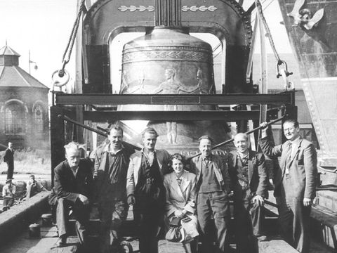 mehrere Personen stehen vor einer großen Glocke