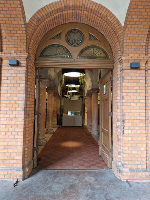 Blick in die Aufbahrungshalle vom Sankt Thomas Friedhof: rote Bodenfließen und Terrakotta-farbige Säulen