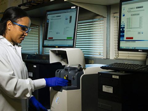 Frau im Laborkittel steht an computergesteuertem Testgerät