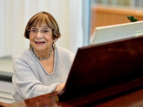 Eine Frau sitzt an einem Piano und lächelt in die Kamera.