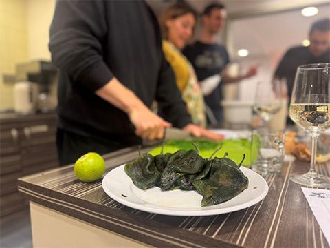 Geschmorte grrüne Paprika im Vordergrund. Im Hintergrunf schneidet ein Mann Kräuter mit einem Messer.
