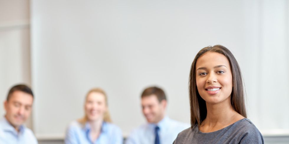 Lächelnde junge Frau im Vordergrund und drei Personen im Hintergrund