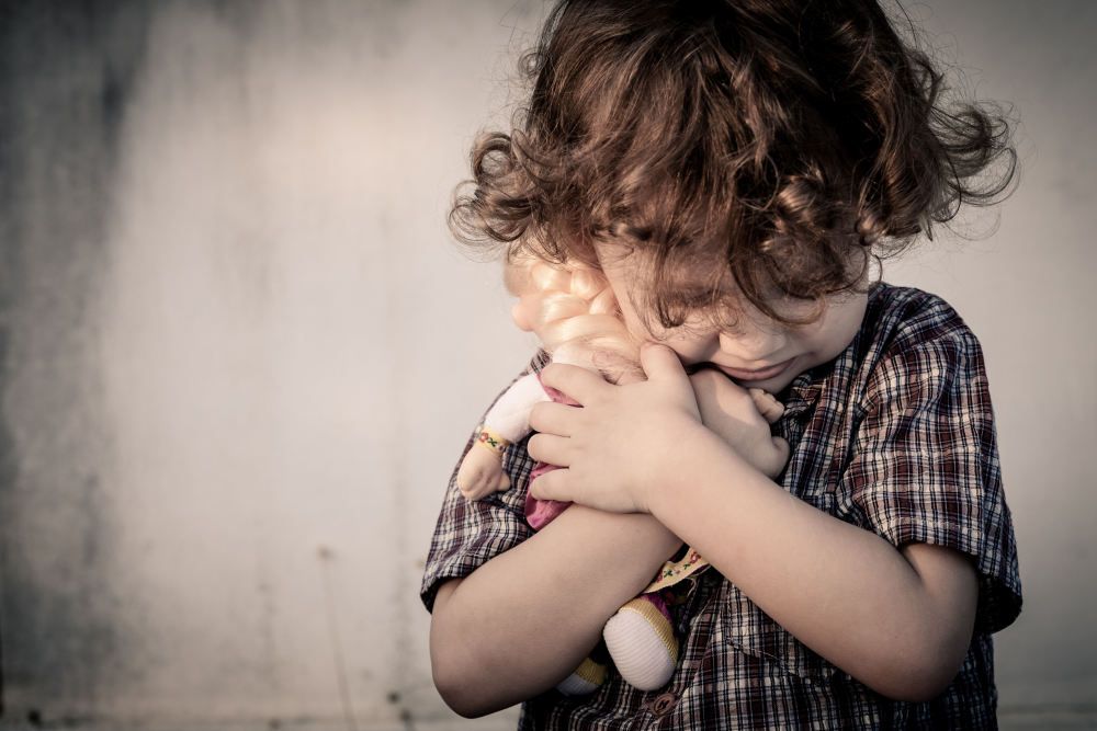 Trauriger kleiner Junge mit Puppe im Arm