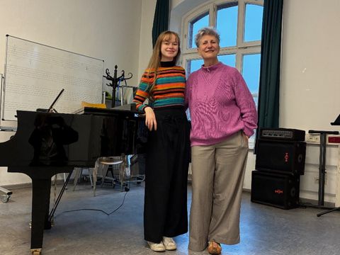 Eine Jüngere und eine ältere Frau posieren für die Kamera vor einem Klavier.