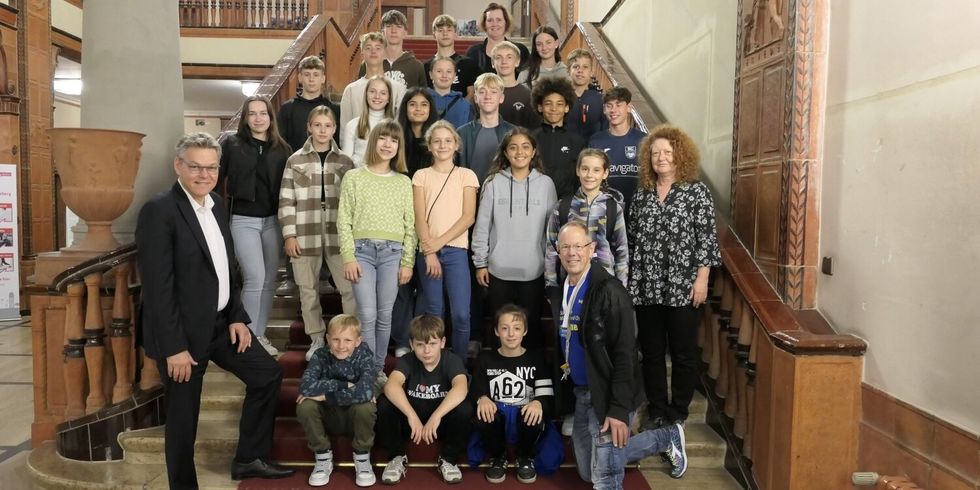 Eine Gruppe Jugendlicher und Kinder stehen und sitzen auf einer Treppe mit drei Erwachsenen.