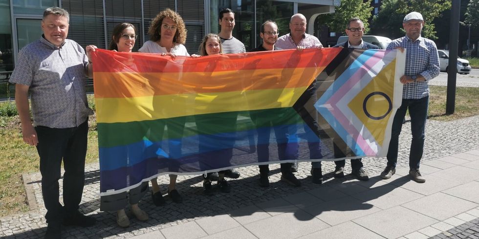 Bezirksamtsmitglieder und Mitarbeitende des Bezirksamtes halten die progressive Regenbogenfahne