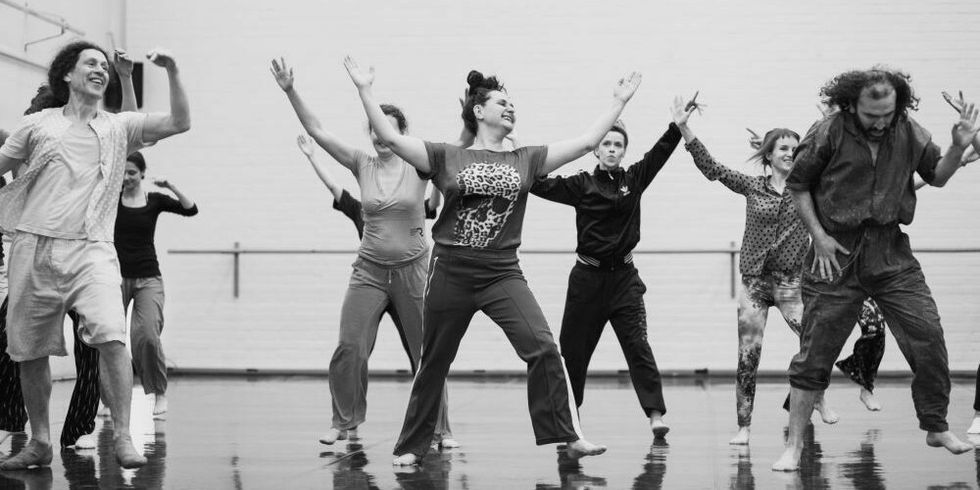 Eine schwarz-weiß Fotografie von einer tanzenden Menschengruppe in einer Halle.