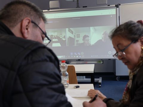 Kursteilnehmende vor Monitor mit Online-Teilnehmenden