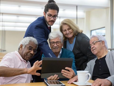 Vier Senior*innen und ein junger Mann schauen gemeinsam auf ein Tablet
