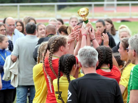 Ein Mädchenteam jubelt und streckt den gewonnenen Pokal in die Höhe.