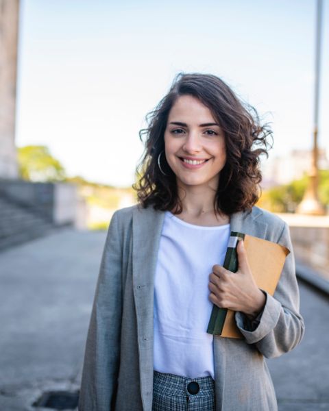 Frau mit Buch vor einem Universitätsgebäude
