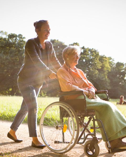 Junge Frage schiebt eine Seniorin in einem Rollstuhl durch einen Park