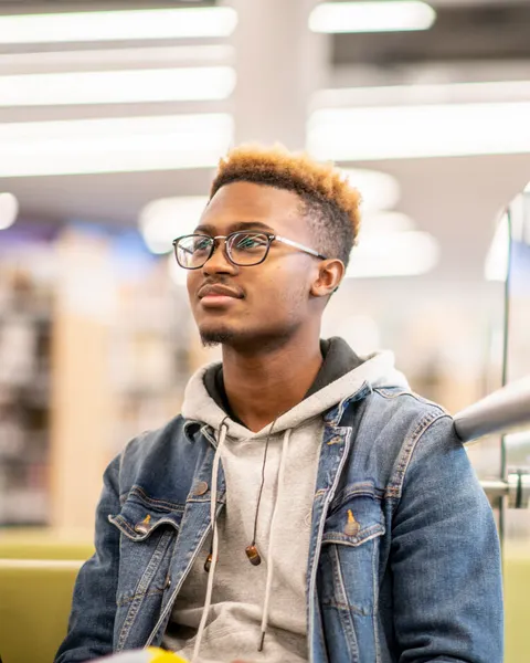 Ein Mann mit Brille und Buch in der Hand sitzt auf einer Bank in einer Bibliothek