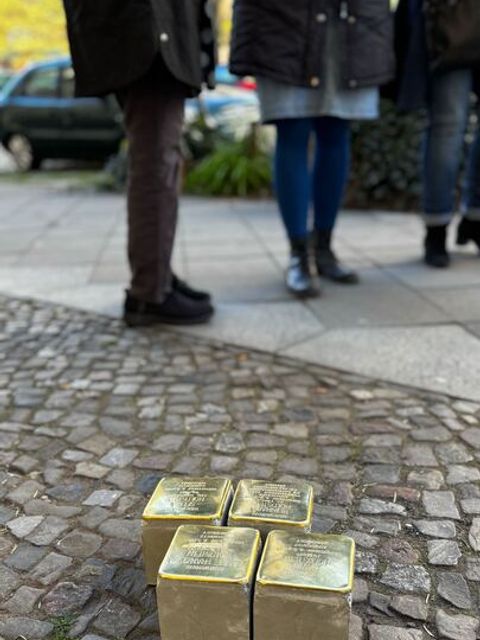 Noch nicht verlegte Stolpersteine auf Pflastersteinen mit 3 Personen im Hintergrund