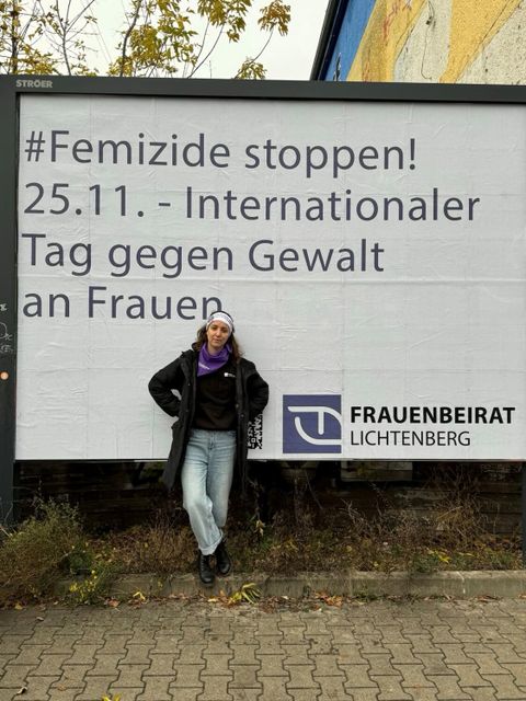 Gleichstellungsbeauftragte Eva Karpf vor der Werbefläche mit dem Text: # Femizide stoppen! 25.11. Internationaler Tag gegen Gewalt an Frauen, in der Nähe einer Tankstelle in der Siegfriedstraße.