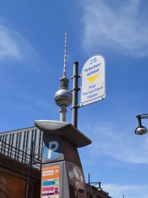 Parkscheinautomat mit dem Bahnhof Alexander Platz und dem Fernsehturm im hHintergrund.